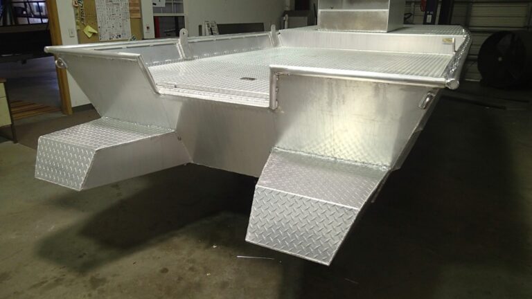 Stern of a bare aluminum work hull with a diamond-plate deck and two stepped pods, in the shop
